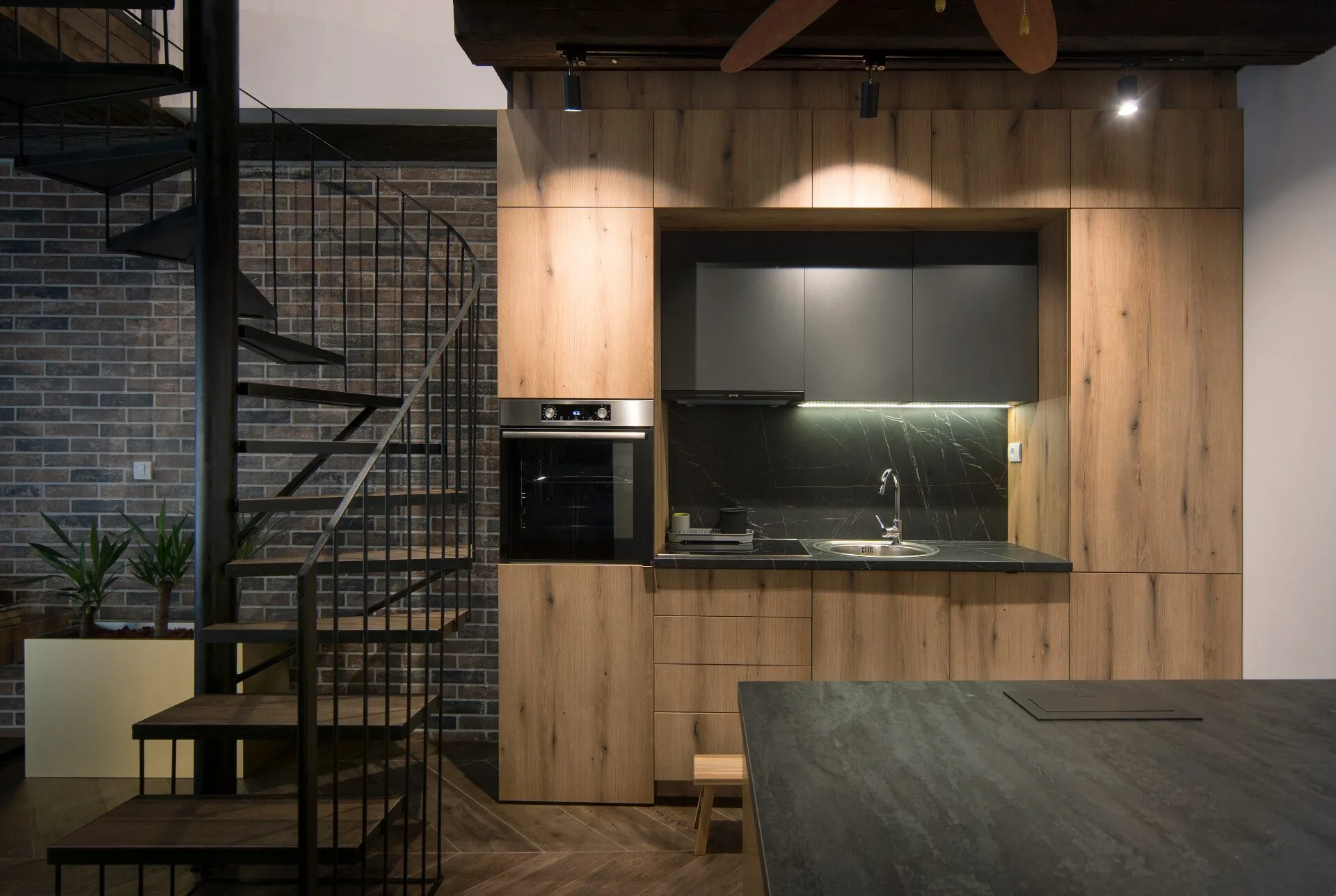 Wooden kitchen with black spiral staircase and brick wall